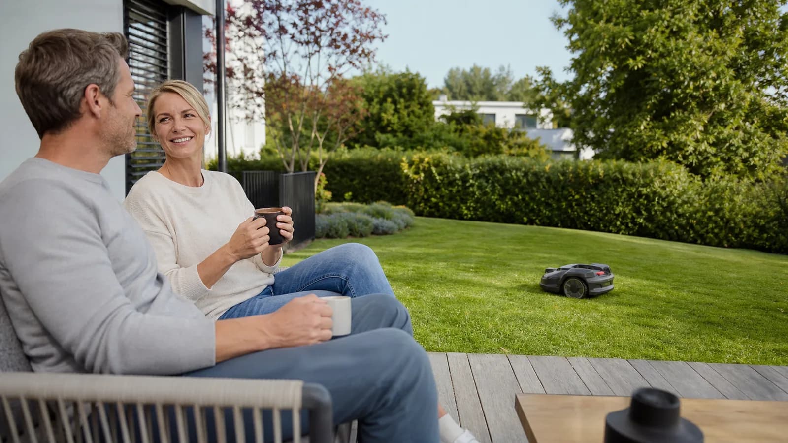 Paar auf einer Terrasse mit Mähroboter im Garten